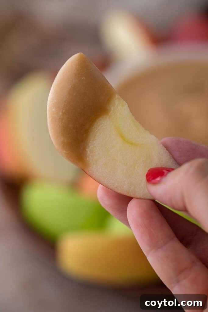 A hand holding an apple slice generously coated in rich, homemade caramel sauce.