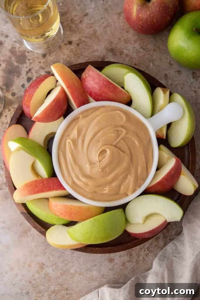 A beautiful wooden serving board featuring a bowl of homemade caramel sauce surrounded by crisp, sliced apples and a few whole apples, ready for dipping.