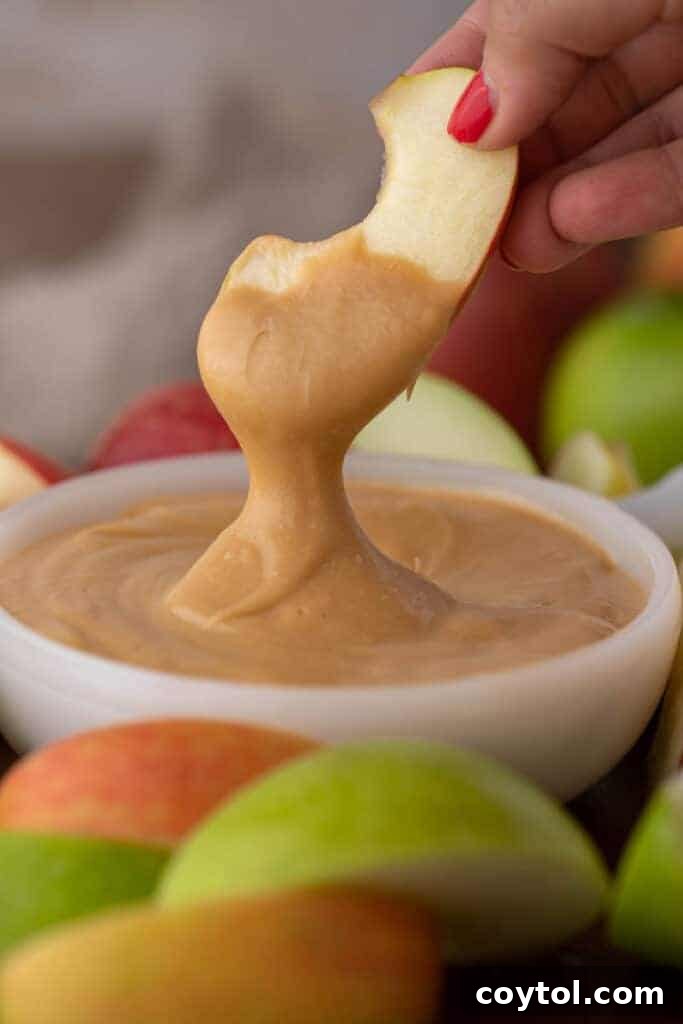 A close-up of a crisp red apple dipped generously in a rich, golden caramel sauce, showcasing its glossy texture.