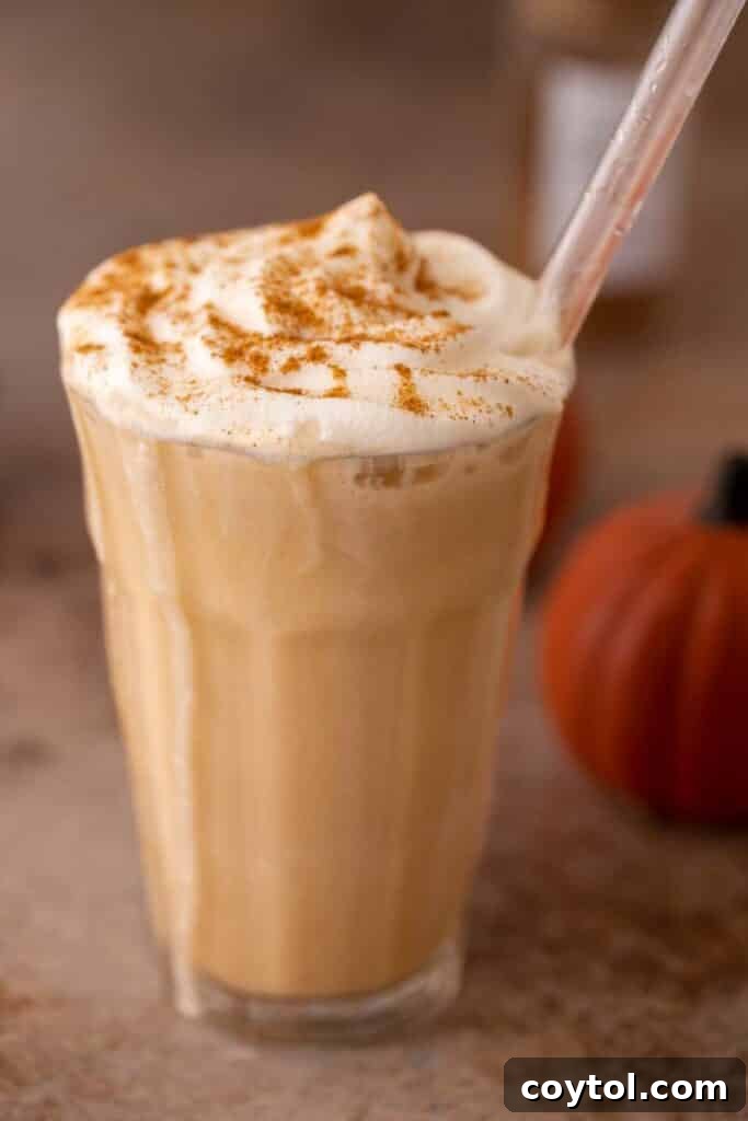 Homemade Starbucks Pumpkin Spice Frappuccino in a tall glass, topped with whipped cream and a sprinkle of pumpkin spice, evoking autumn vibes.