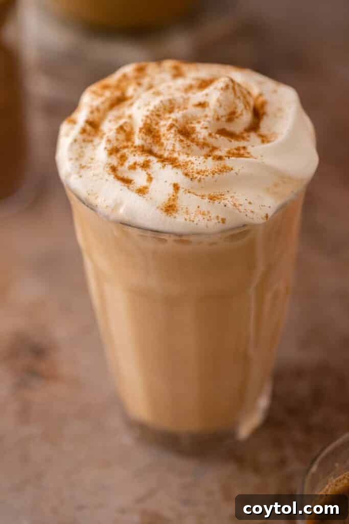 Close-up of a frothy Starbucks Pumpkin Spice Frappuccino in a glass, with whipped cream and pumpkin spice topping.
