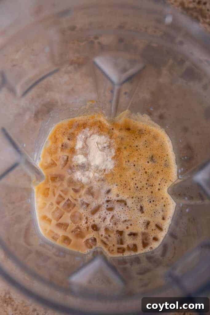 Ice, coffee, milk, and pumpkin spice sauce being added to a blender for a pumpkin frappuccino.