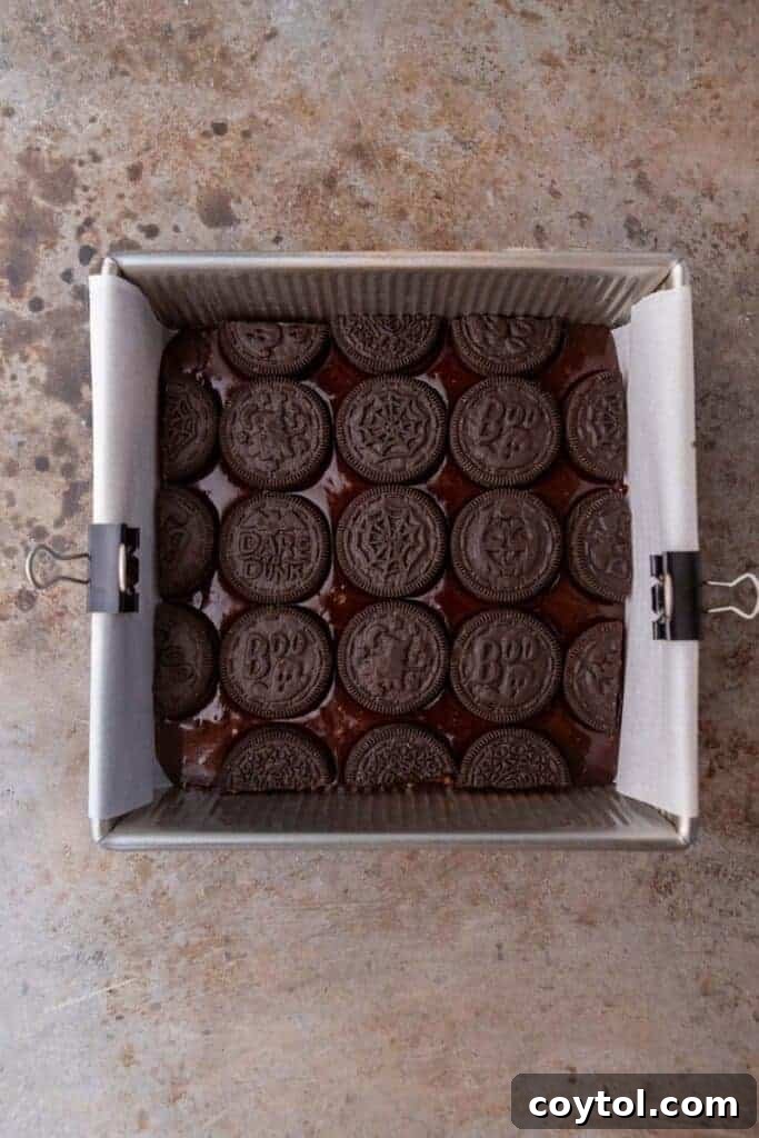 Layer of Halloween Oreos arranged over a base of brownie batter in a baking pan