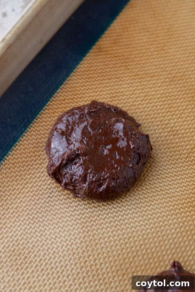 Scooped portions of brownie cookie dough placed on a parchment-lined baking sheet, evenly spaced and ready for baking.