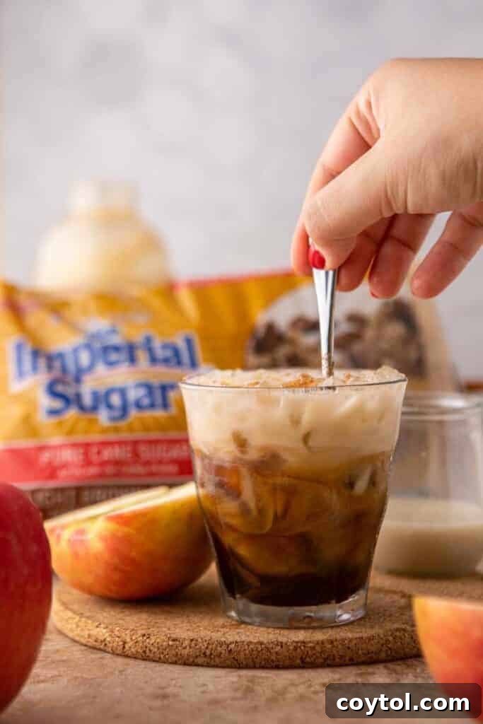 Starbucks Iced Apple Crisp Oatmilk Shaken Espresso 12 A hand stirring a glass of homemade Starbucks Iced Apple Crisp Oatmilk Shaken Espresso, showcasing the creamy texture and inviting colors.