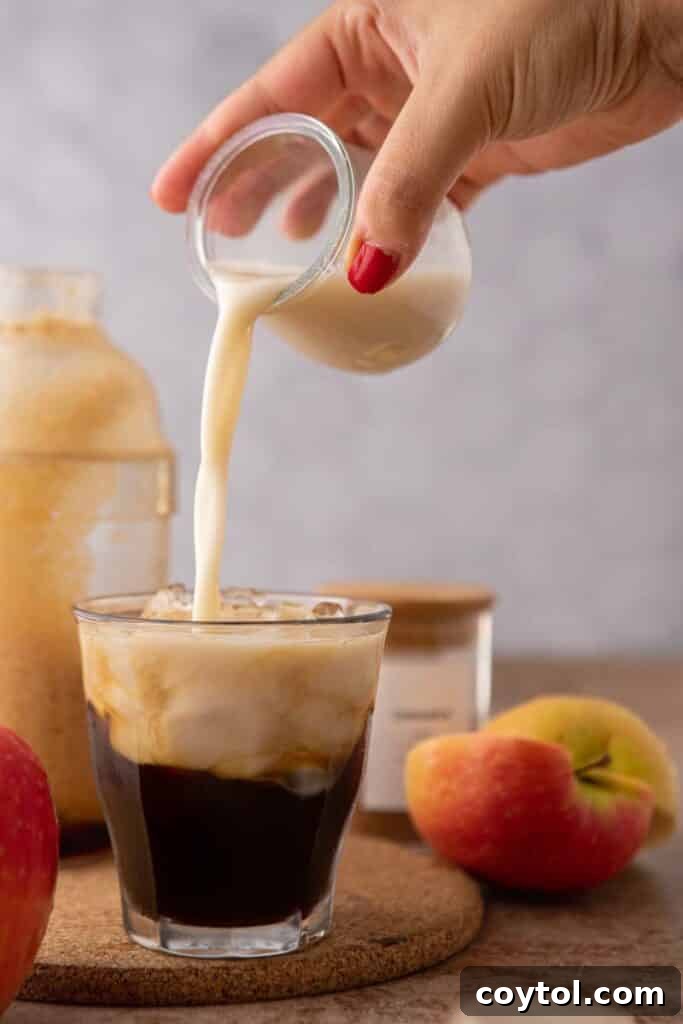 Starbucks Iced Apple Crisp Oatmilk Shaken Espresso 9 Creamy oat milk being gently poured over the espresso base in a glass, creating beautiful layers for the apple crisp shaken espresso.