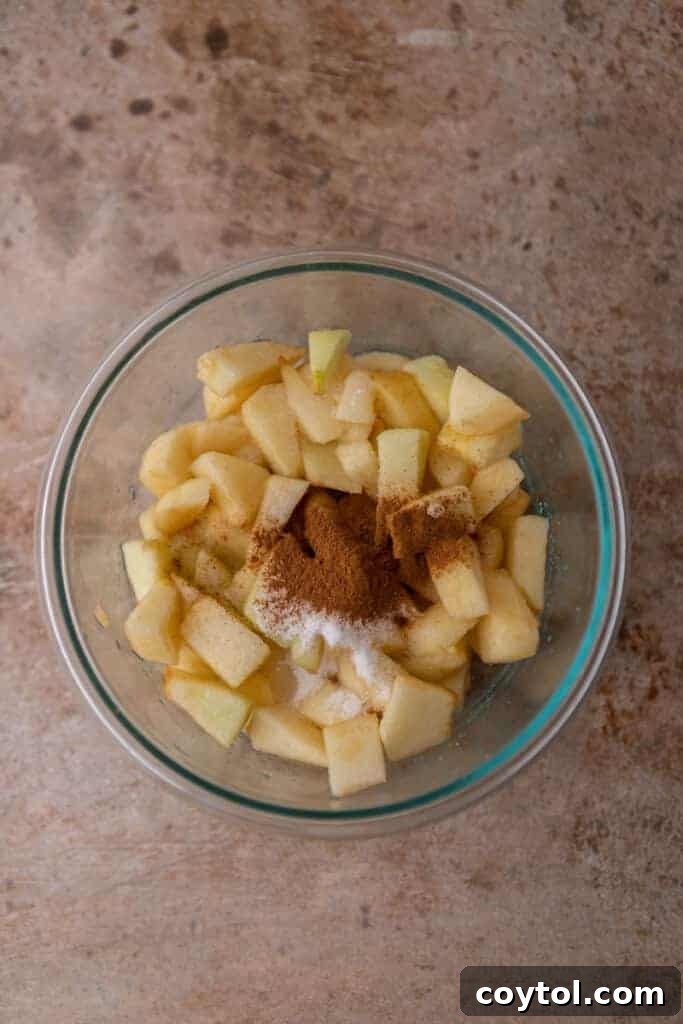 Cubed apples generously coated with cinnamon and sugar in a bowl, ready to become the flavorful apple layer for the cheesecake bars.