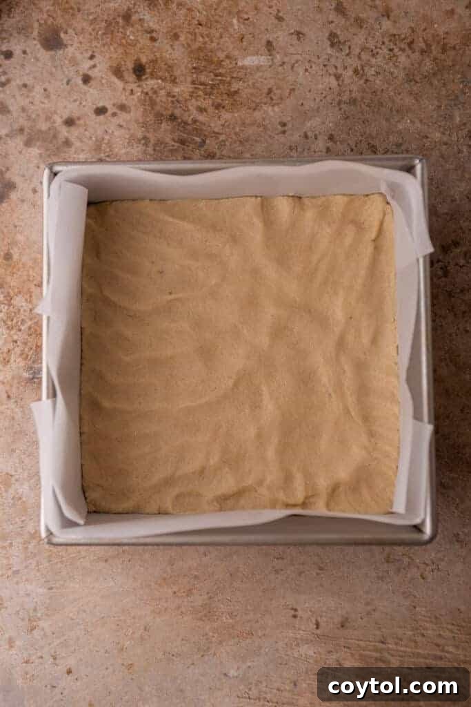 Smooth shortbread cookie dough pressed evenly into an 8x8 inch baking pan, ready for its initial bake.