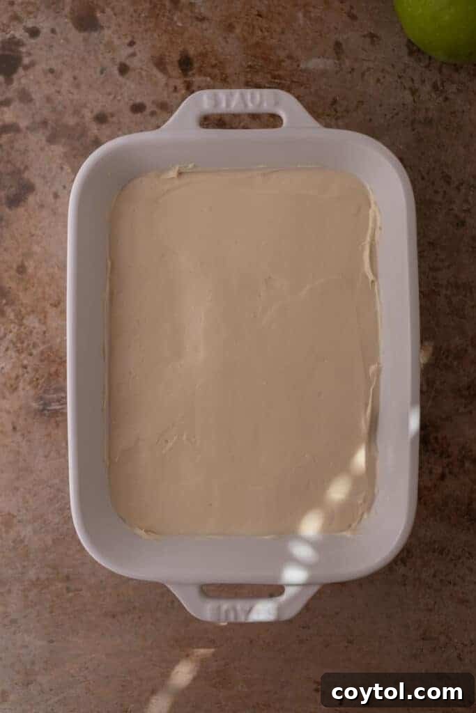 Cheesecake layer spread evenly in a baking pan, ready for caramel