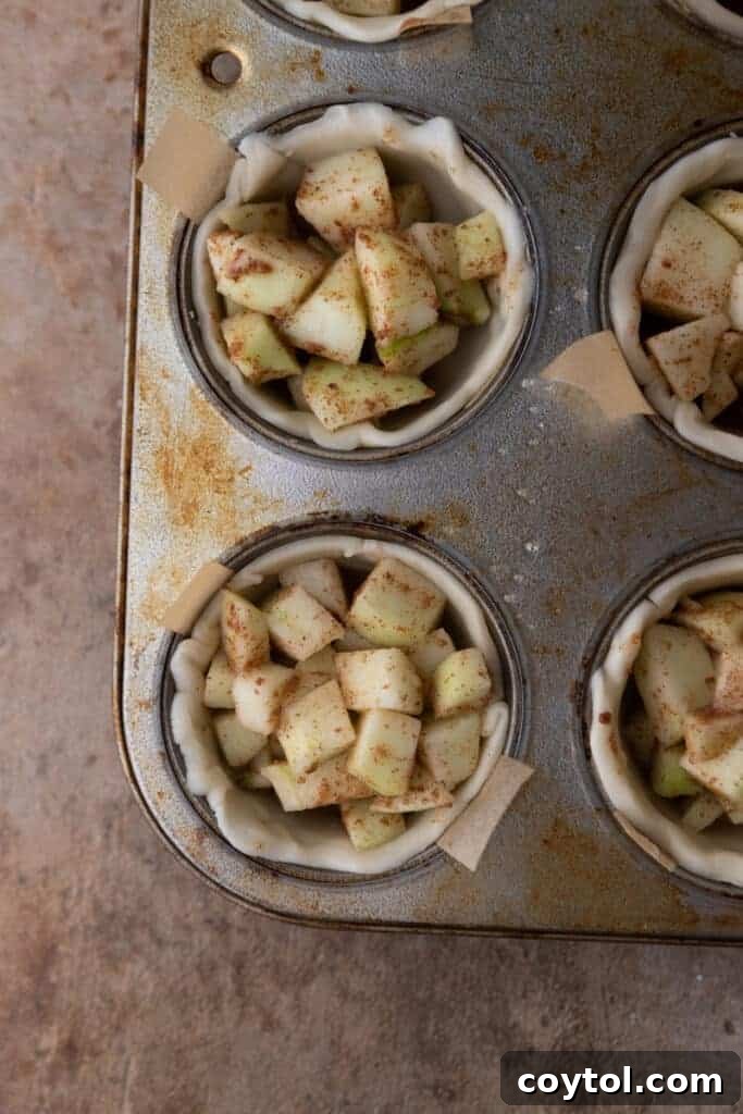 unbaked apple sitting in pie shells in a muffin tin