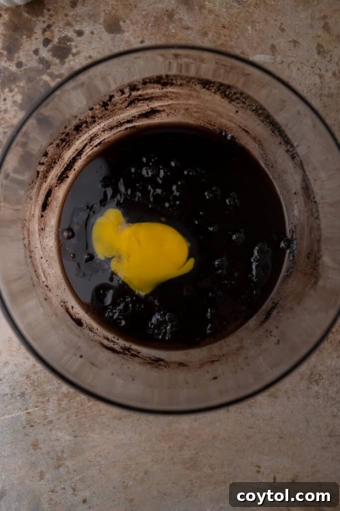 Dark cocoa brownie batter with an egg being mixed in.