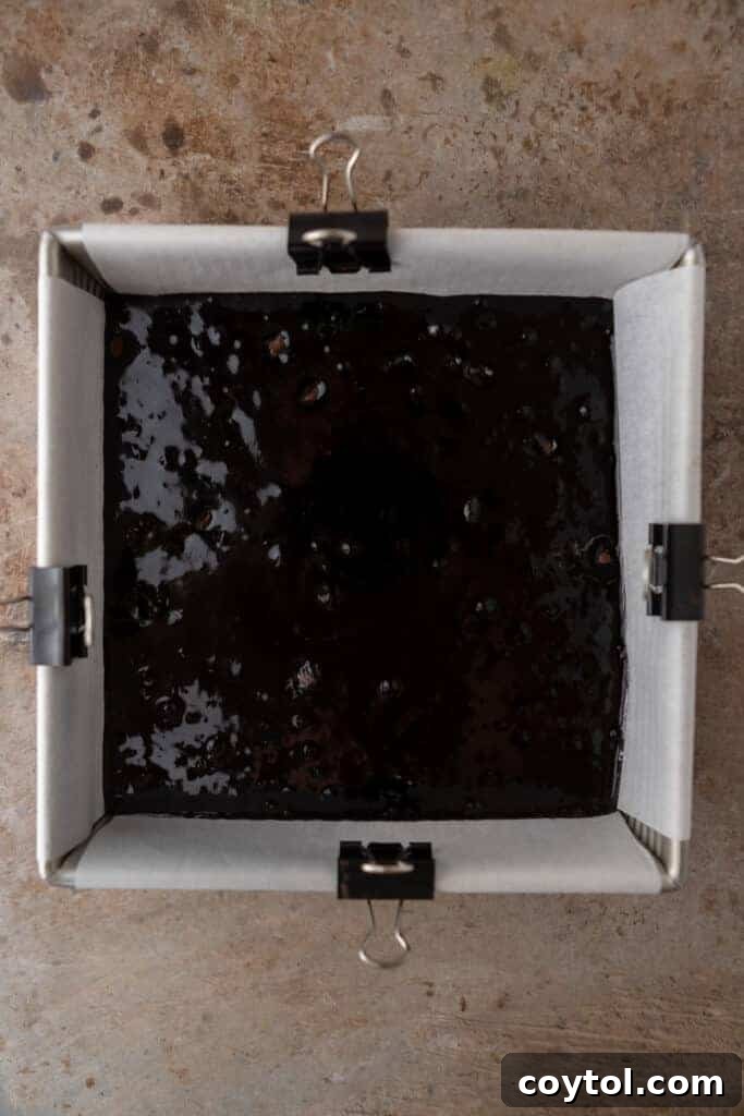 Black cocoa brownie batter spread evenly in a parchment-lined baking pan.