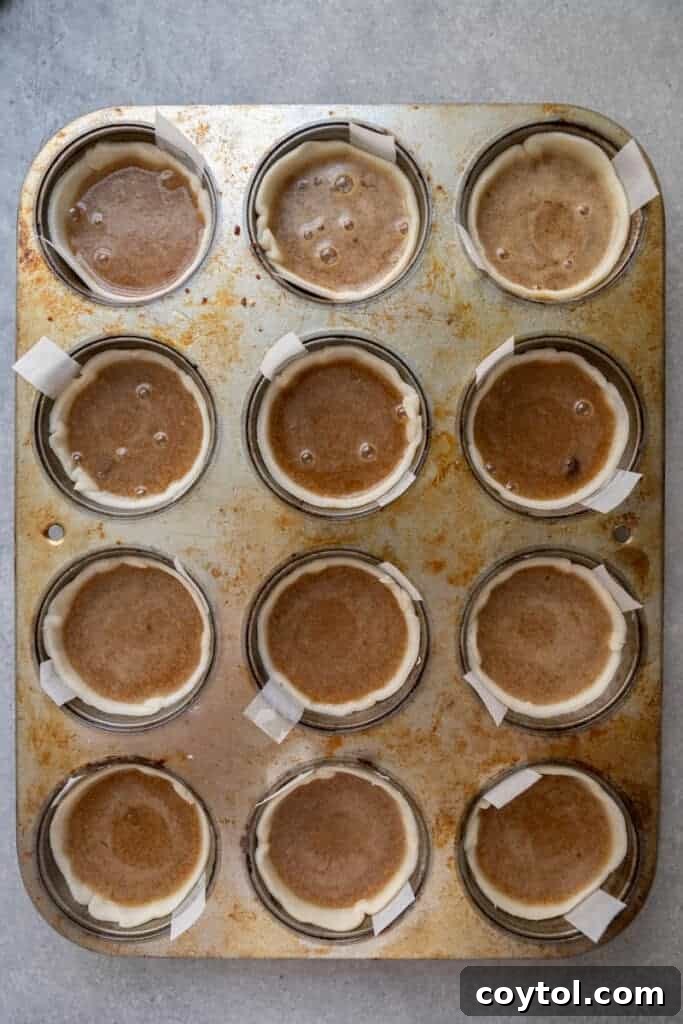 Unbaked butter tarts in a muffin tin, filled with the rich custard mixture