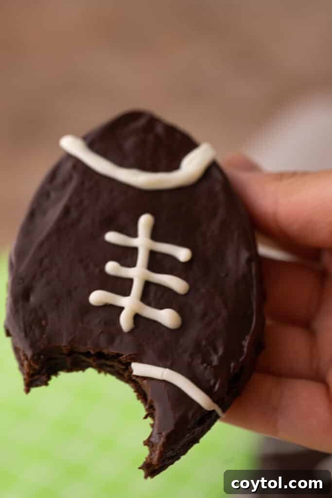 A hand proudly holding a perfectly shaped football brownie, showcasing its delicious chocolate coating and white laces.