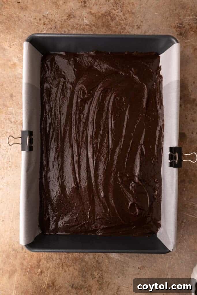 Smooth brownie batter spread evenly in a parchment-lined baking pan, ready for the oven.