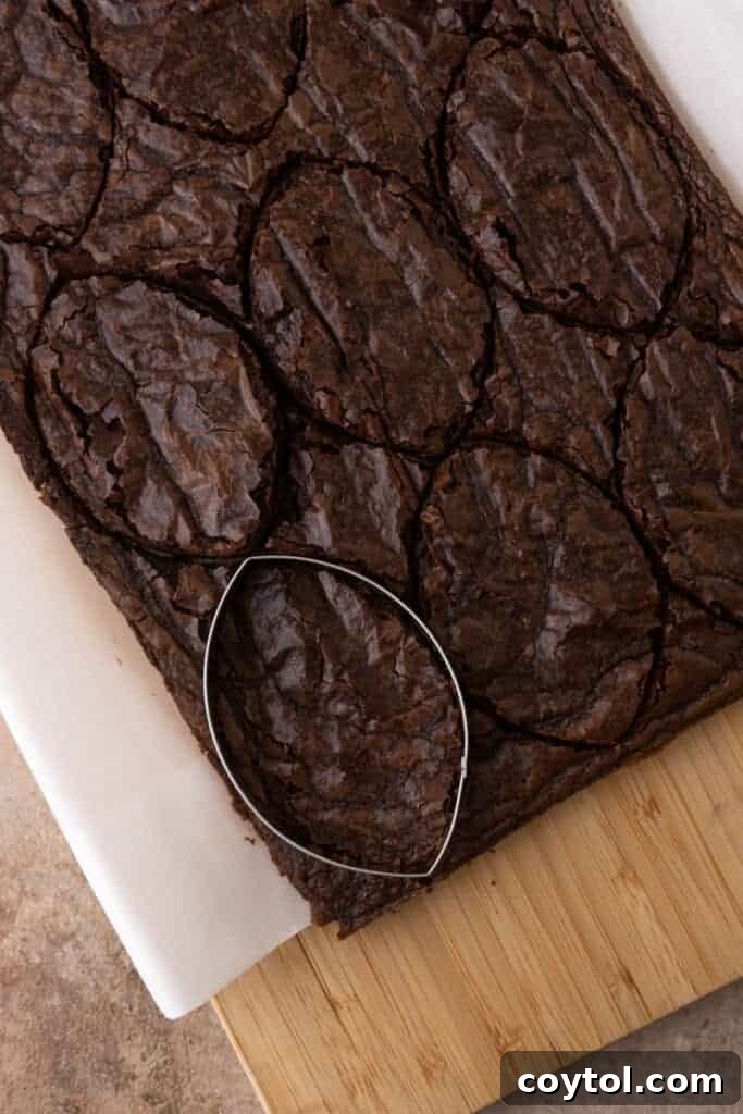 A football-shaped cookie cutter pressing into a baked brownie, creating perfect game-day treats.