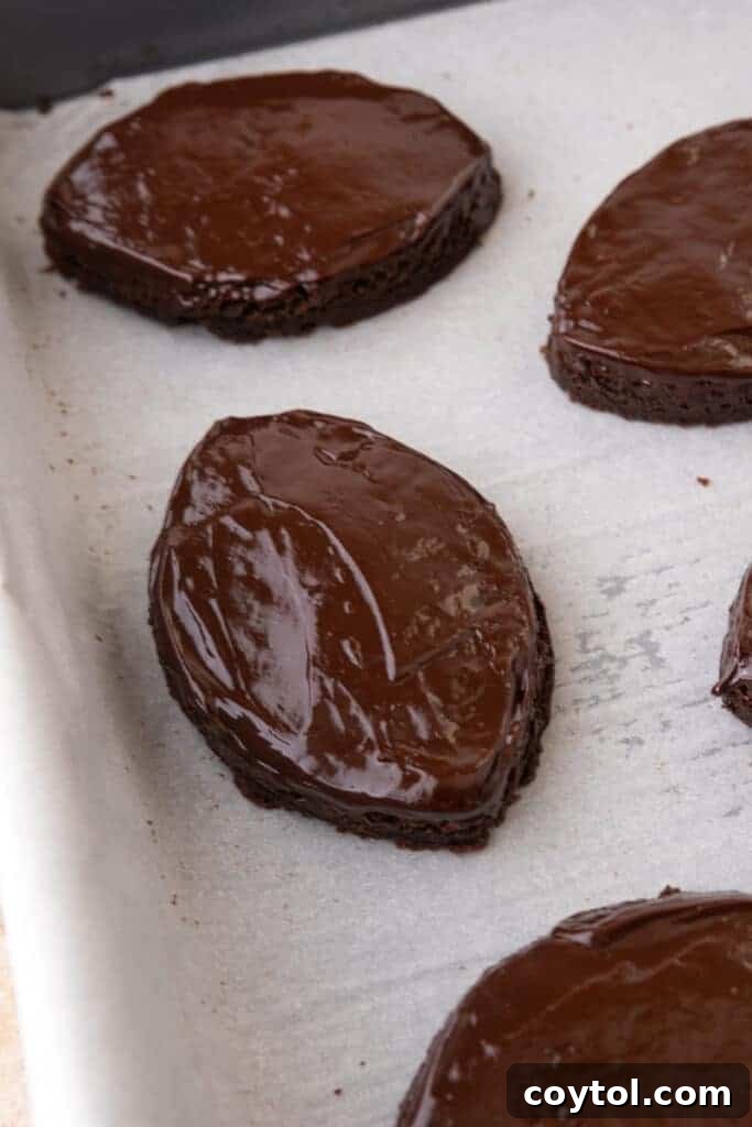 Football-shaped brownies dipped in shiny chocolate ganache, laid out on parchment paper to set.