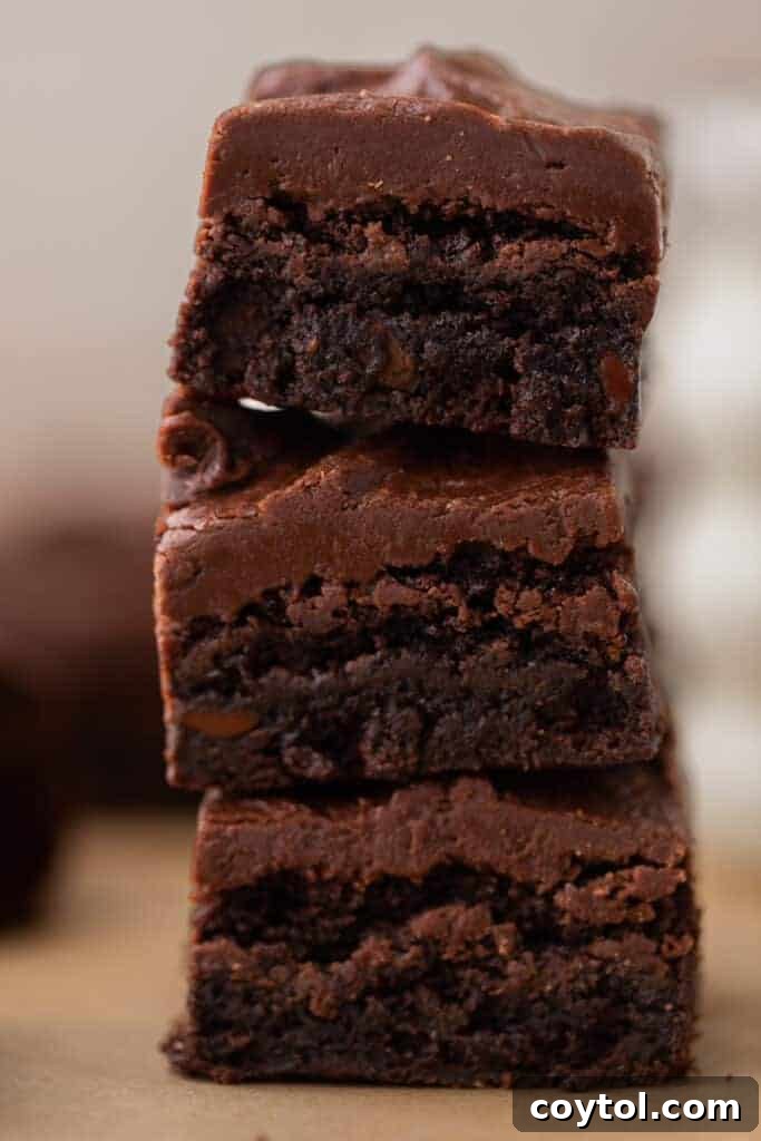 The 4-Minute Frosting Hack for Brownies 6 Three decadent brownies, generously layered with rich chocolate frosting, stacked elegantly on a plate.