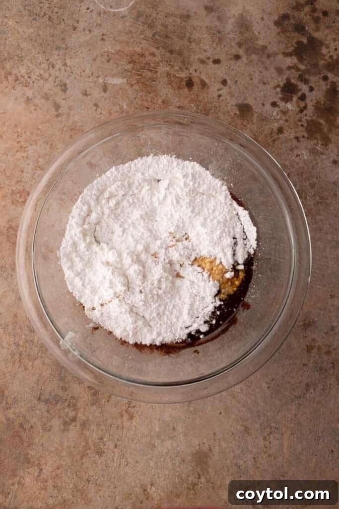 The 4-Minute Frosting Hack for Brownies 9 Powdered sugar being added to the melted butter and cocoa mixture in a bowl, a key step for the brownie frosting recipe.