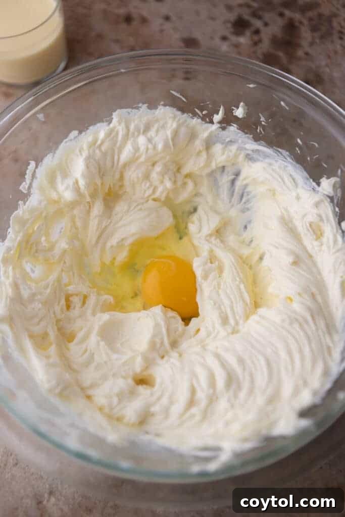 Creamed cream cheese and eggs being mixed in a bowl for the cheesecake filling.