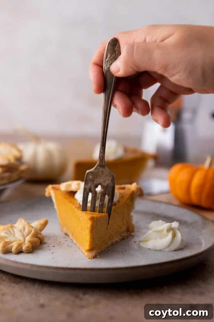 A delicious slice of pumpkin pie on a white plate with a fork, ready to eat