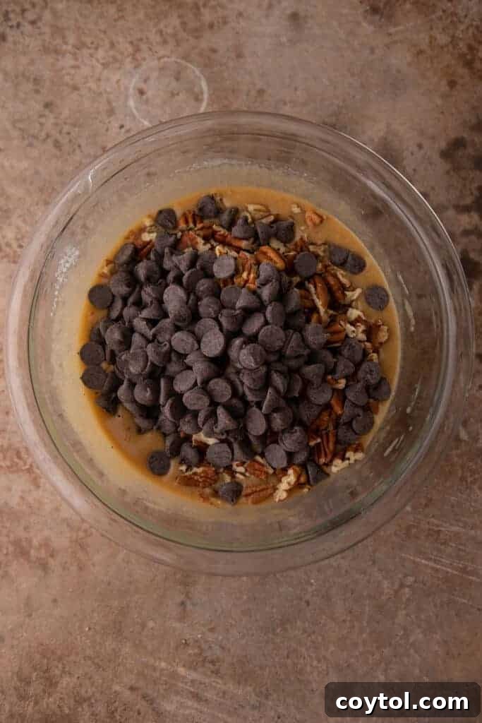 chocolate chips and pecans added on top of raw filling ingredients in a bowl