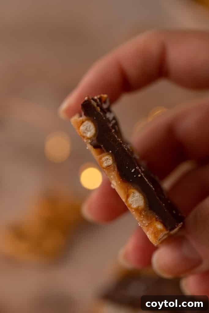 A hand holding a piece of Christmas Chocolate Treat showing the pretzel and caramel layers.