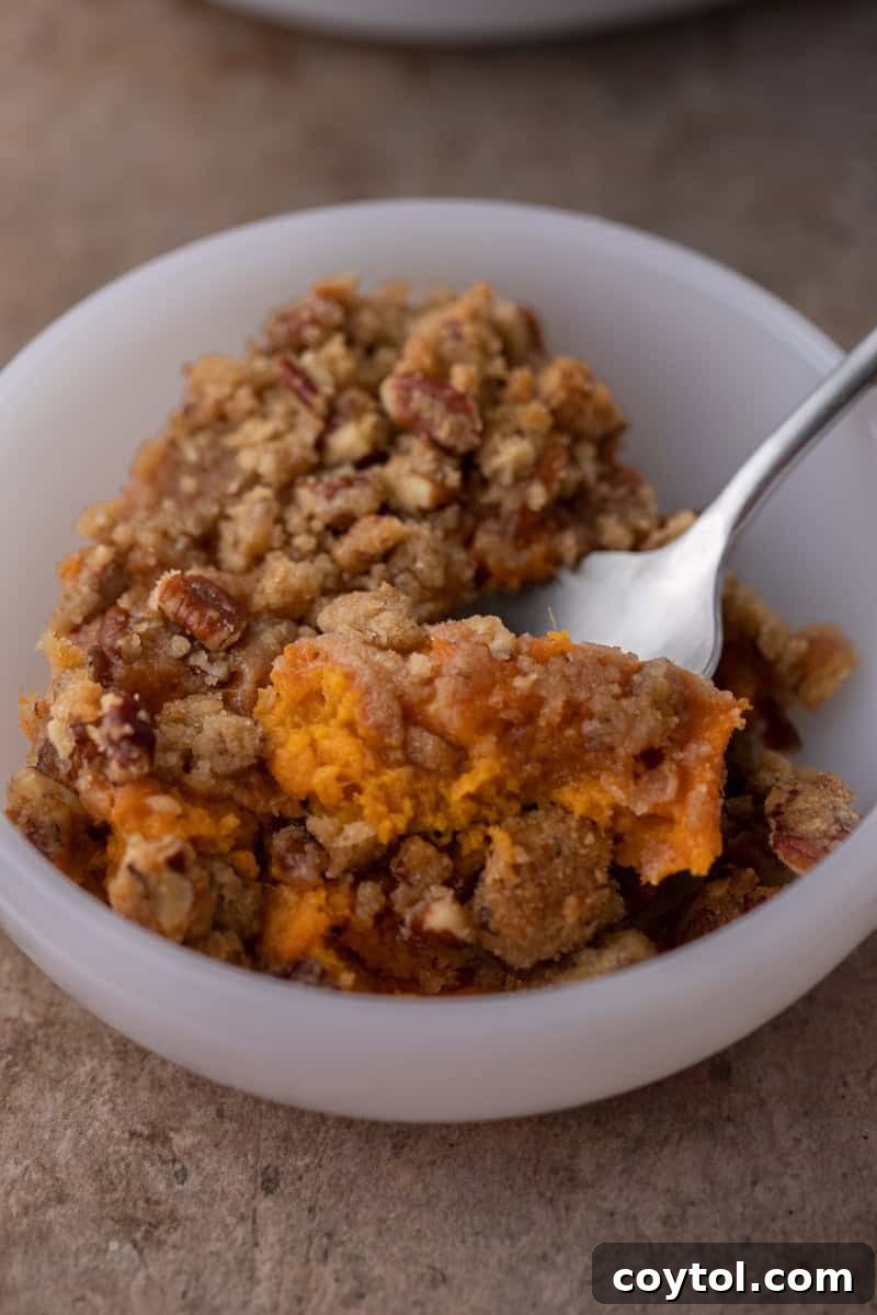 A spoon dipping into a bowl full of sweet potato casserole, revealing its fluffy interior and crunchy pecan topping.