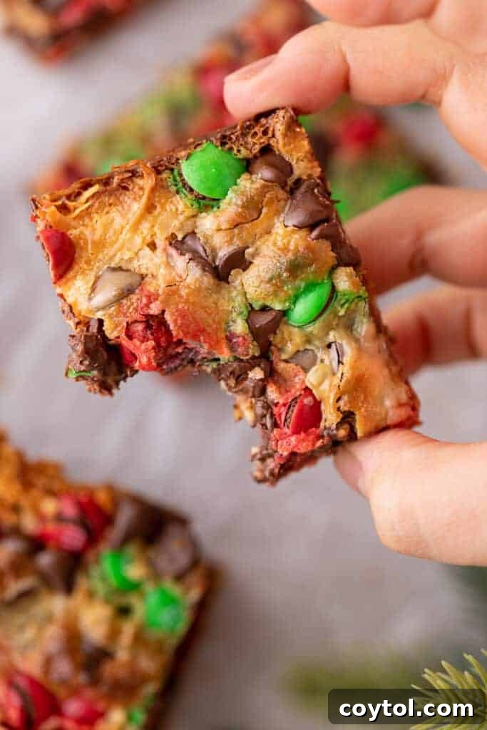 A hand holding a Christmas Magic Cookie Bar with a bite taken out, showing its gooey layers