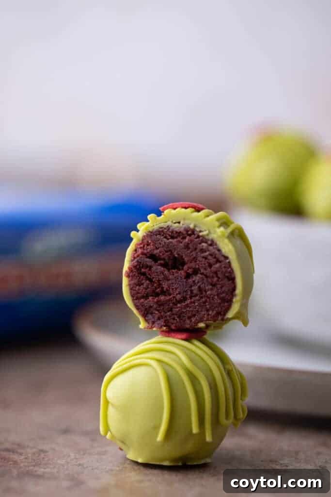 a grinch oreo truffle split in half, on top of a whole one, revealing the red velvet interior