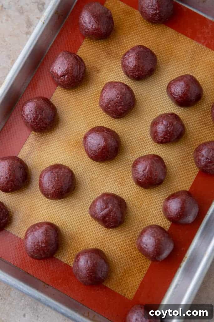 a bunch of rolled out uncoated grinch oreo truffles laid out on a baking sheet, ready for chilling
