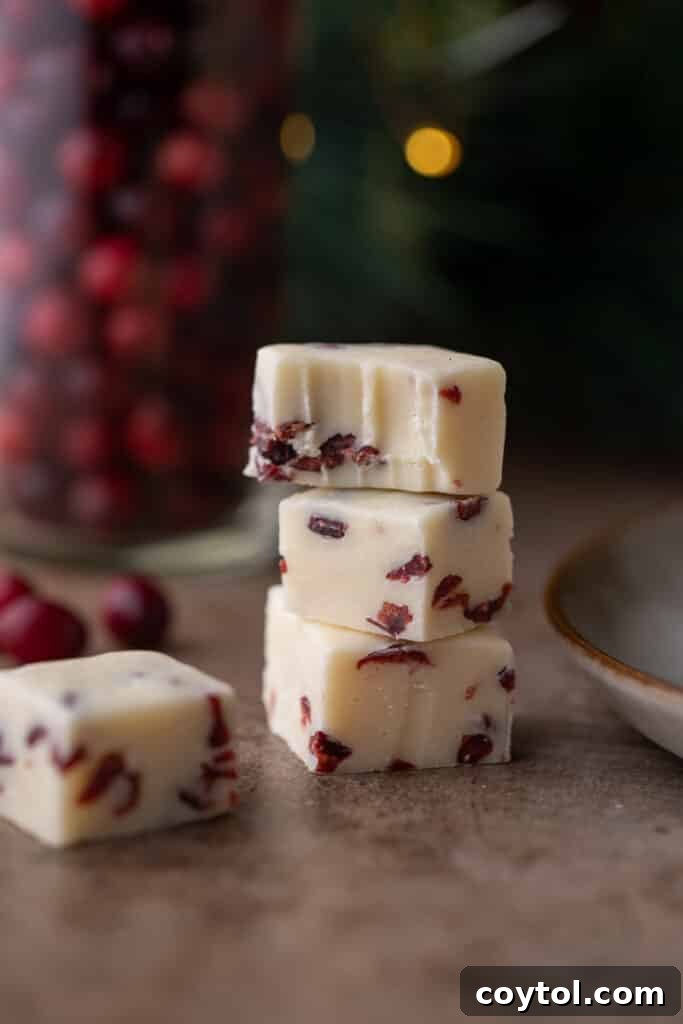 Three stacked cranberry white chocolate fudge squares, with a bite taken from the top one, revealing its soft interior and cranberry pieces.