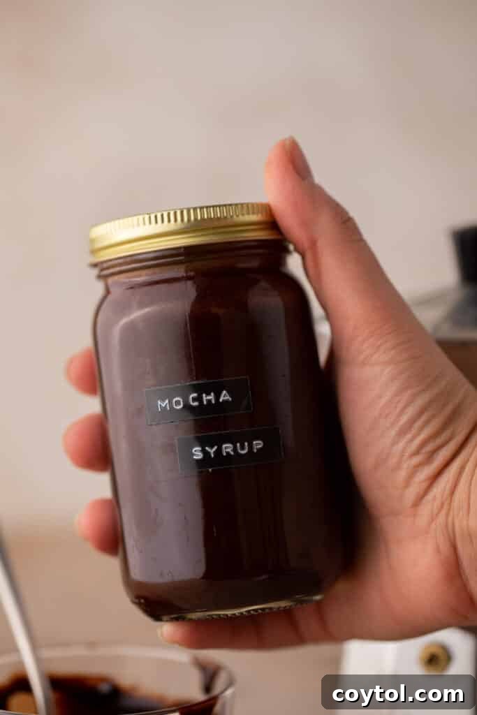Whip Up Perfect Homemade Mocha Syrup 4 A hand holding up a mason jar filled with freshly made homemade mocha coffee syrup.
