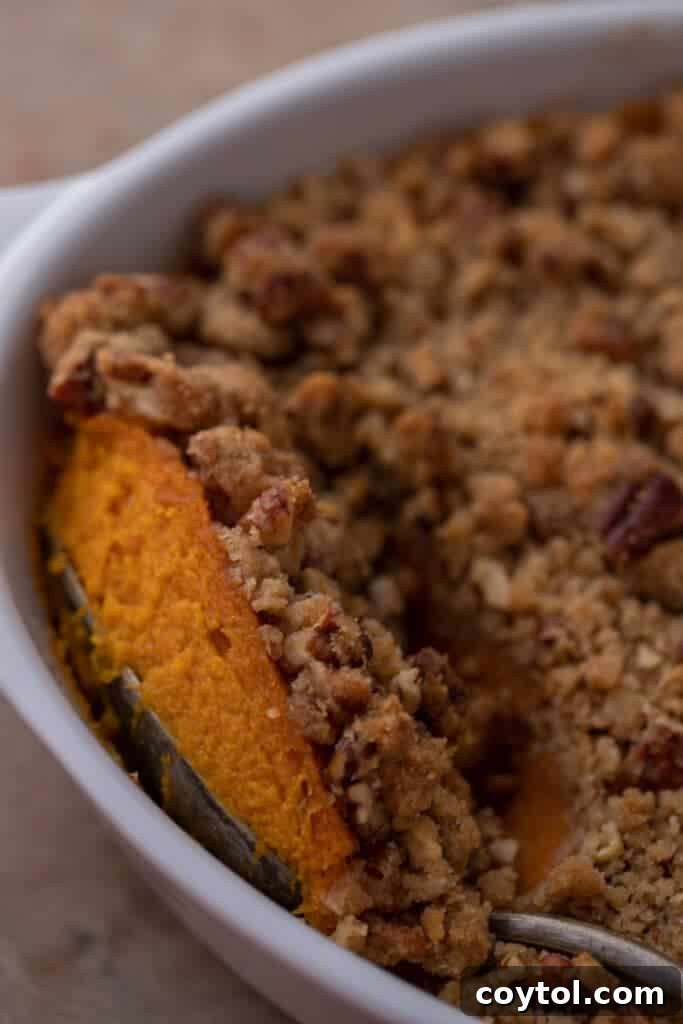 A spoonful being taken from a rich, golden sweet potato casserole topped with a crunchy pecan streusel, ready to be served at Thanksgiving dinner.