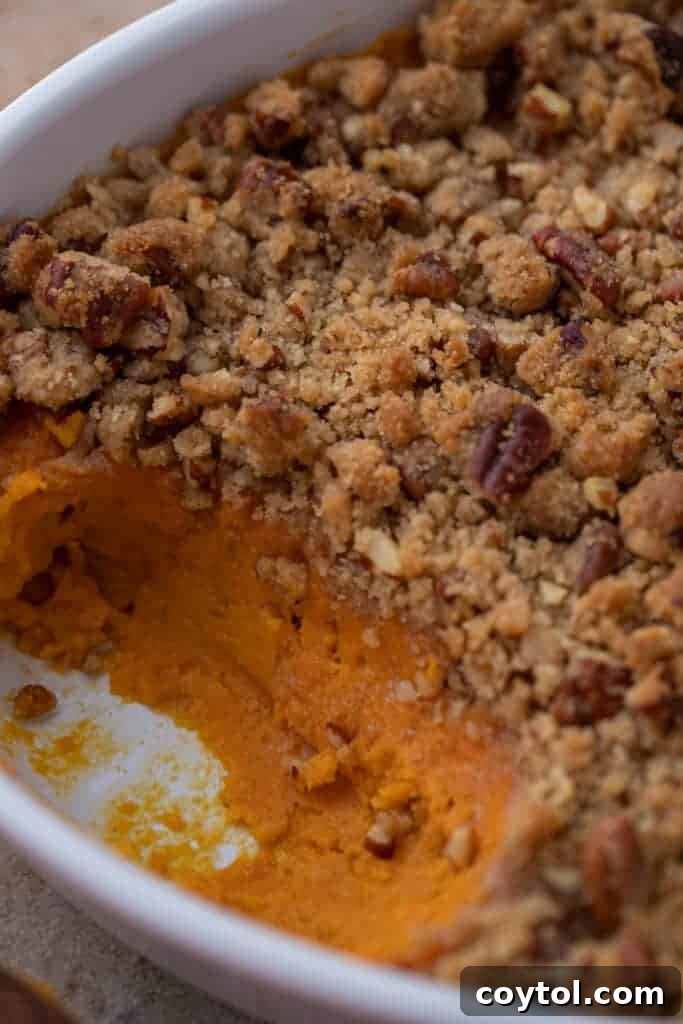 A large serving of sweet potato casserole with pecan topping, with a section scooped out, revealing the creamy interior.