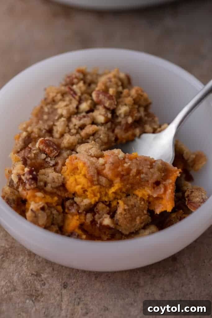 A spoon resting in a bowl full of creamy sweet potato casserole topped with golden-brown pecan streusel, ready to be enjoyed.