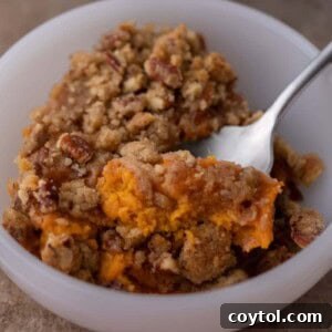 spoon in a bowl full of sweet potato casserole with pecan topping
