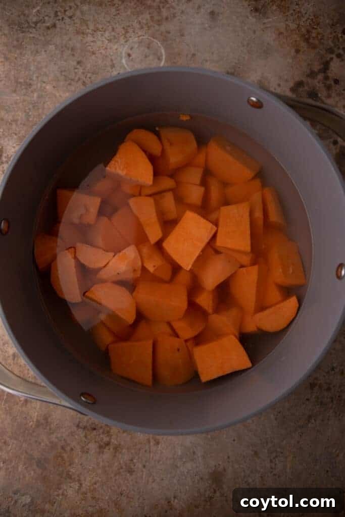 Cubed sweet potatoes boiling in a large pot of water on a stove.