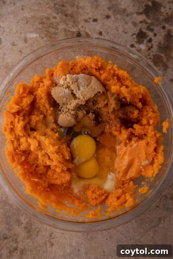 Mashed sweet potatoes in a bowl with other unmixed casserole ingredients, such as butter, eggs, and brown sugar, around the edges.