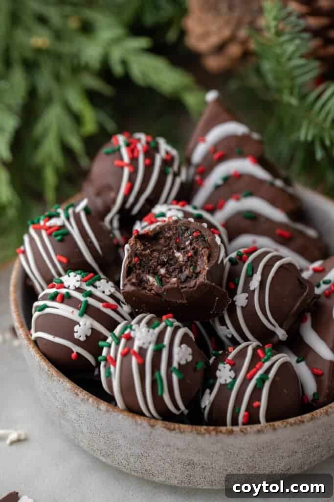 Bowl of chocolate Christmas tree cake truffles topped with white drizzle and sprinkles, with one truffle sliced open.
