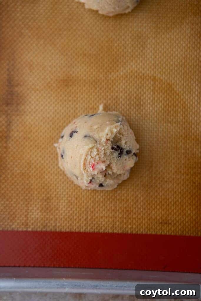 Raw, perfectly scooped cookie dough balls arranged on a parchment-lined baking sheet, ready for the oven.