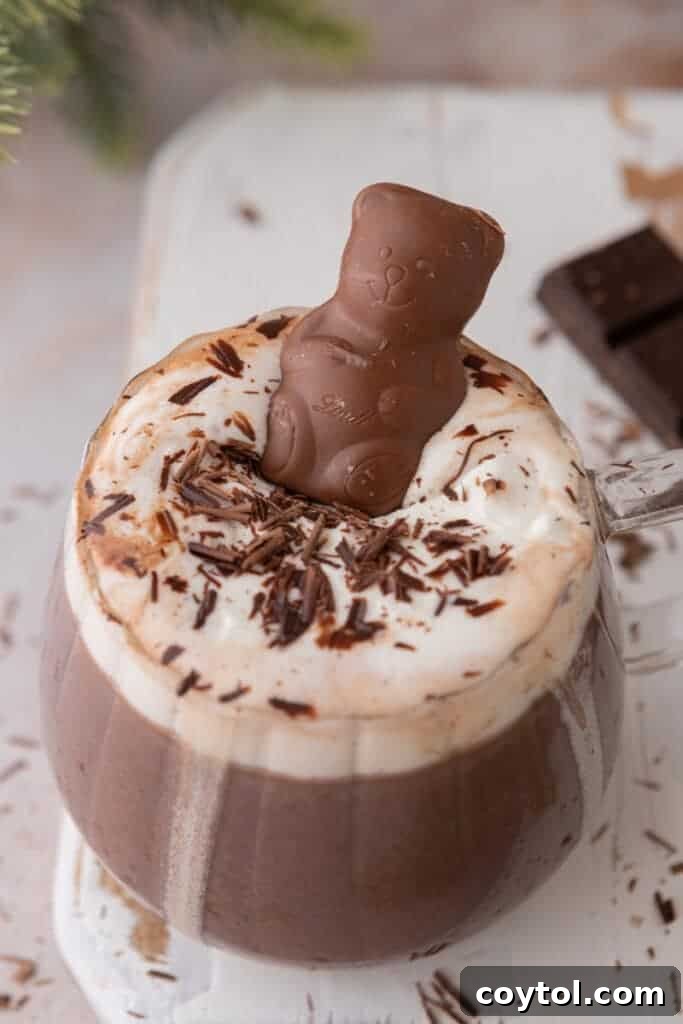 A cute chocolate bear floating on whipped cream in a glass of hot chocolate.