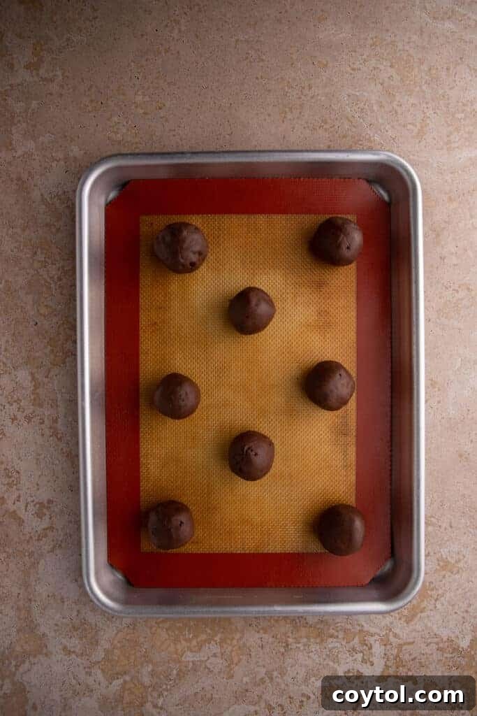 Chocolate cookie dough rolled into balls on a lined baking sheet.