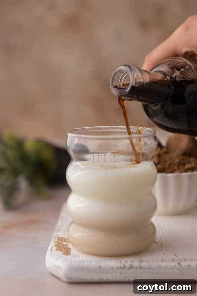 A finished cup of coffee with brown sugar syrup being poured into it, showing the syrup's luscious texture.