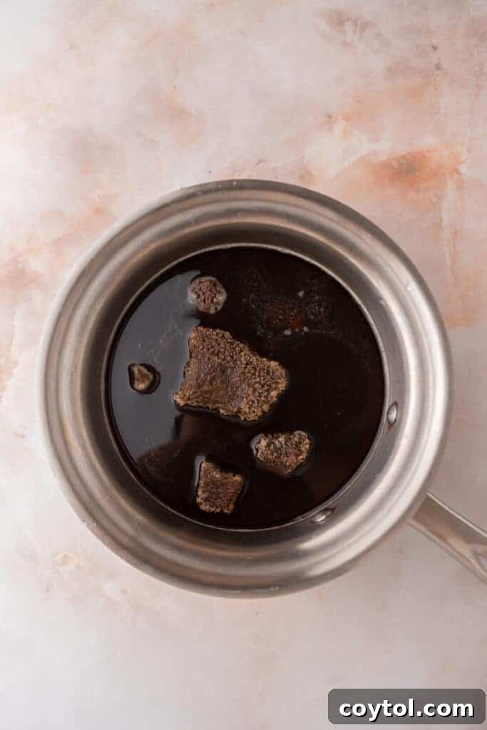 Unmixed ingredients in a saucepan before heating, showing the brown sugar, water, and cinnamon stick.