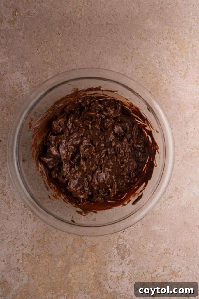 Mixed pretzels and peanuts in melted chocolate in a clear bowl