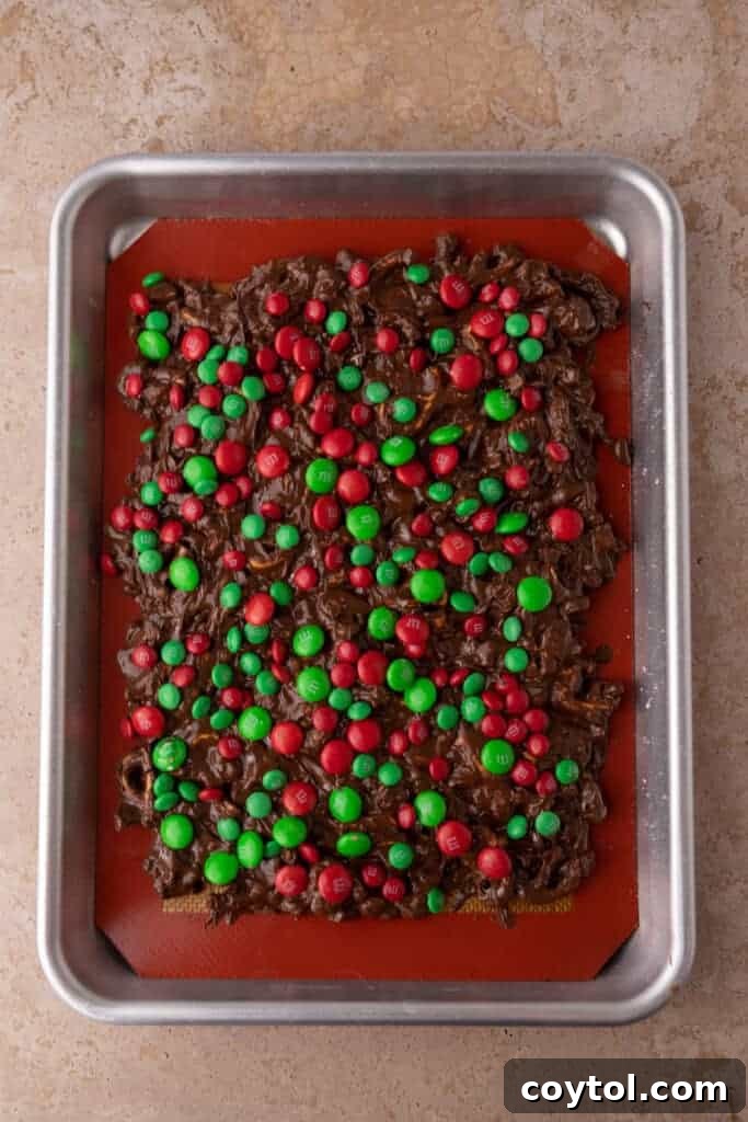 Christmas peanut pretzel M&M's bark mixture spread out evenly on a baking pan