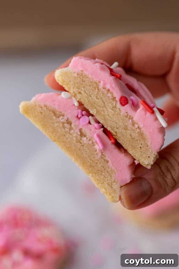 A hand holding a Valentine's Day frosted sugar cookie, neatly cut in half to reveal its soft interior