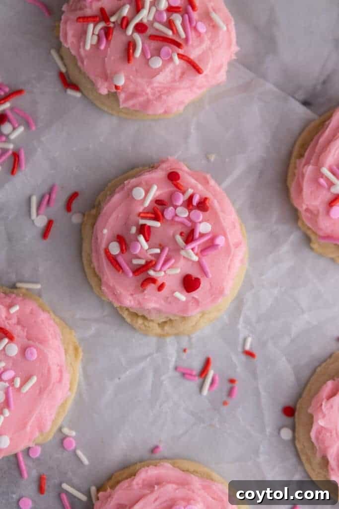Overhead shot of several frosted cookies with vibrant pink frosting and an array of festive sprinkles