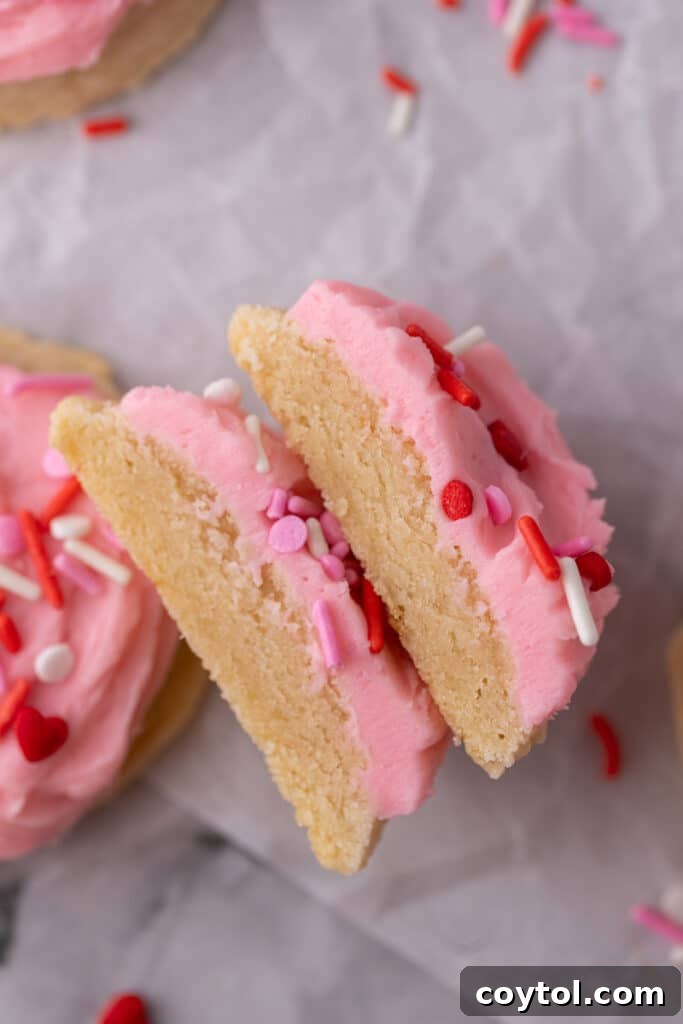A Valentine's Day frosted sugar cookie sliced neatly in half, showcasing the perfect cookie texture and thick frosting